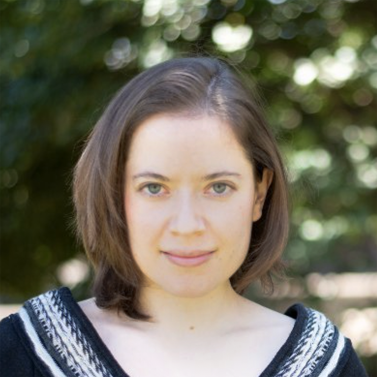 Isabel Estevez, Senior Advisor at Public Renewables Project, standing outdoors with a soft-focus green background, wearing a black and white patterned top.